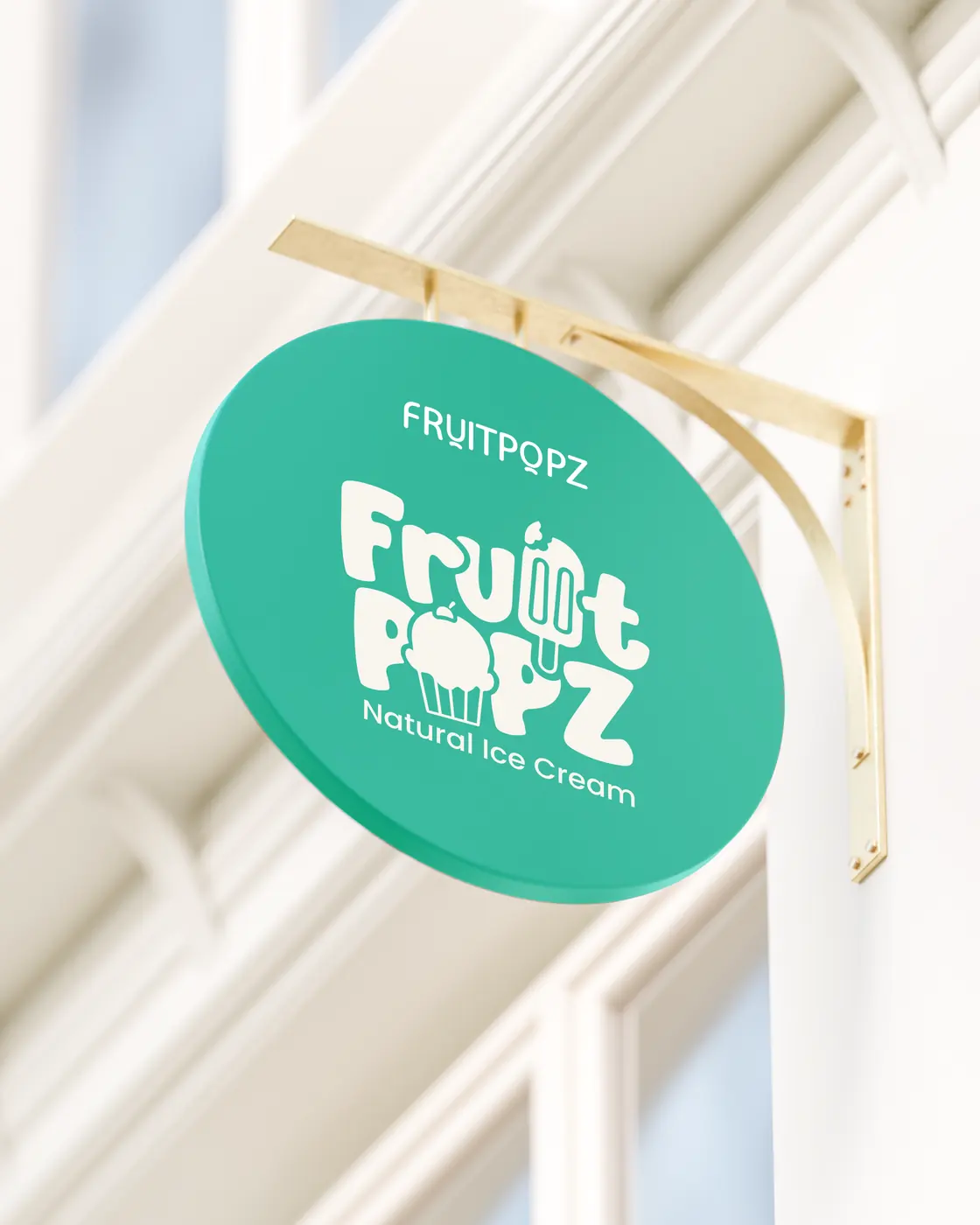 A round aqua Fruitpopz sign hanging from a brass bracket on a cream shopfront.