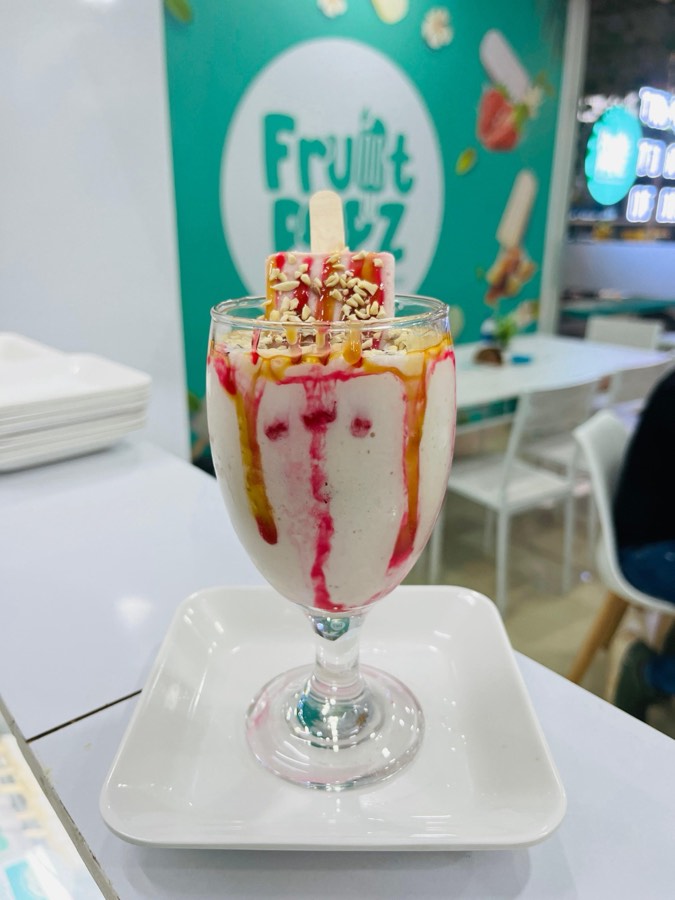 A tall Fruitpopz sundae in a glass with strawberry and caramel sauce, crushed nuts, and a popsicle standing in the top.